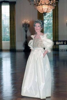 an older woman in a white dress standing in a large room with chandeliers