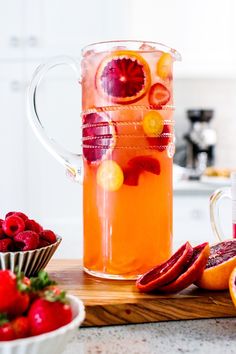 a pitcher filled with liquid sitting on top of a counter next to sliced oranges and strawberries