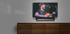 a flat screen tv mounted on the wall above a wooden entertainment center with a guitar