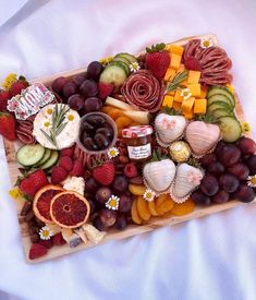 a wooden platter filled with assorted fruits and veggies on top of a white sheet