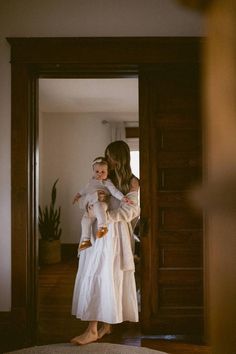 a woman holding a baby in her arms while standing in front of a doorway with an open door