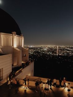 people are standing on top of a building at night with the city lights in the background