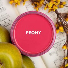 a pink tin with the word peony on it next to some apples and flowers