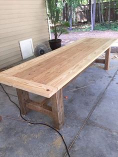 a long wooden table sitting on top of a cement floor in front of a house