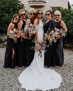 a group of women standing next to each other wearing black dresses and holding bouquets