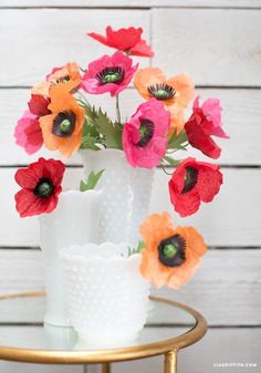 an arrangement of red, orange and pink flowers in a white vase on a table