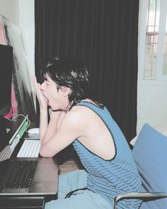 a woman sitting at a desk in front of a laptop computer with her hand on her face