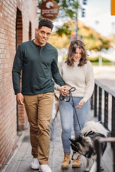 a man and woman are walking their dog down the street with one holding on to his leash