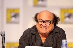 an older man sitting at a table with a book in front of him and a microphone