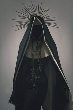 a woman wearing a black cape with spikes on her head and necklaces around her neck