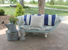 a bench with a pillow and watering can on the ground in front of a tree