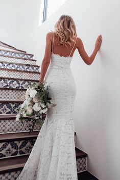 a woman in a white wedding dress is standing on some stairs and looking down at her bouquet