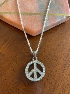 Peace Sign Pendant Necklace. The necklace features a silver peace sign pendant inlayed with white rhinestones on the front. The pendant is in good condition, but shows small signs of wear due to its age. There is normal surface wear on the back of the pendant where part of the silver coating has worn away to reveal the copper alloy backing underneath. There are also small signs of wear on the bail that attaches the pendant to the chain. The pendant is suspended from a new pure silver plated figa Peace Necklace, Peace Sign Necklace, Rare Jewelry, Gifts For My Girlfriend, Sign Necklace, Buddha Pendant, Friend Necklaces, Long Pendant Necklace, Crystal Necklace Pendant