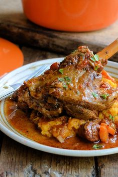 a white plate topped with meat covered in gravy and carrots next to an orange pot