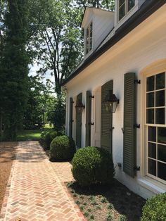 a white house with green shutters and brick walkway leading to the front door area