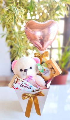 a teddy bear in a gift box with chocolates and heart shaped balloon on the table