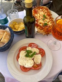 a plate with tomatoes and mozzarella on it next to some bread, wine bottles and glasses