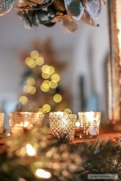 some candles are sitting on a table near a christmas tree with lights in the background