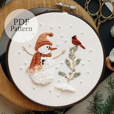 a close up of a embroidery on a hoop with a snowman and two birds