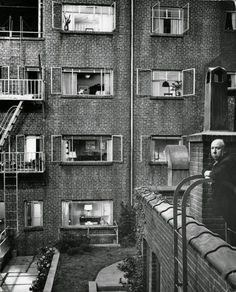 black and white photograph of an old man standing in front of a tall brick building