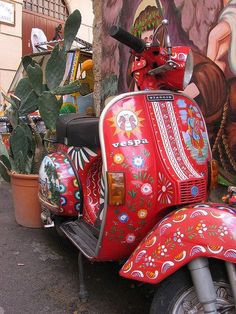 a red scooter parked in front of a wall with paintings on it's side