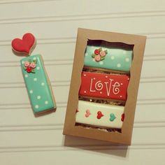 two decorated cookies in a cardboard box next to a cookie with the word love on it