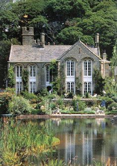 a large house sitting on top of a lush green hillside next to a lake and forest