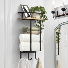 towels are stacked on a shelf next to a mirror and potted plant in a bathroom