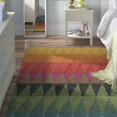 a room with a bed, dresser and colorful rugs on the floor in front of it