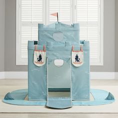 a child's play castle with two doors and windows in the background, sitting on a blue rug