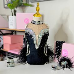 a black and gold dress with feathers on display in front of some pink jewelry boxes