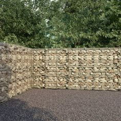 a stone wall is shown in the middle of a parking lot with gravel and trees behind it