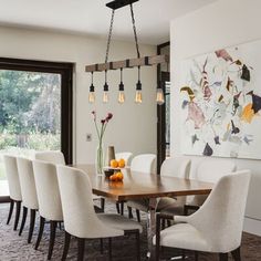 a dining room table with white chairs and an art work on the wall behind it