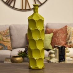 a green vase sitting on top of a wooden table in front of a couch and clock