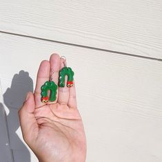 a person is holding two green earrings in their hand and the other one has a red heart on it