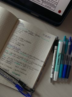 an open notebook sitting on top of a table next to pens