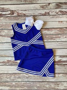 two pieces of blue and white cheerleader outfit on wooden floor with bow at the top