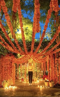 a man standing in front of an orange flower covered archway with candles on the ground