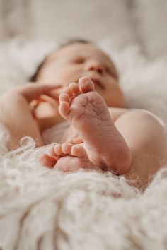 a baby laying down on top of a white blanket with his hands up in the air