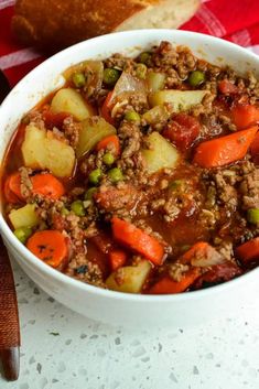 a bowl filled with meat and vegetables next to a loaf of bread on a table