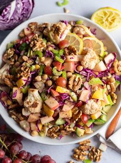 a white bowl filled with salad next to sliced lemons and red cabbage on a table