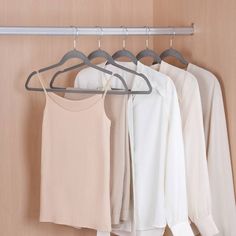 three shirts hanging on a clothes rack next to a white shirt and beige blouses