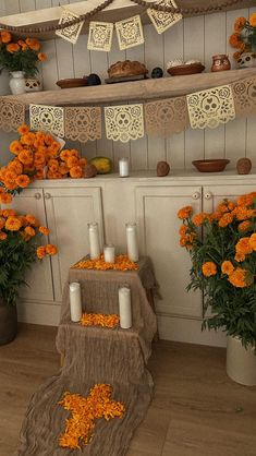 an arrangement of flowers and candles on display in a room with white walls, wood flooring and hanging decorations