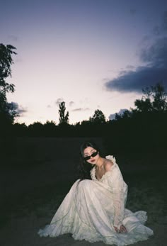 a woman in a white dress sitting on the ground at night with her eyes closed