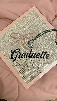 a graduation cap that is on top of a pink blanket with the word graduate written in cursive writing