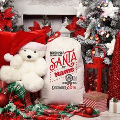 a white teddy bear wearing a santa hat sitting next to presents and christmas tree decorations