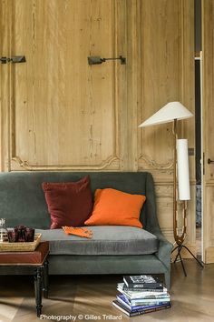 a grey couch with orange pillows in a living room next to a wooden paneled wall