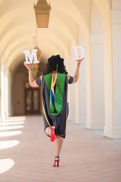 a woman in a graduation gown is running with her letter m on one hand and the other