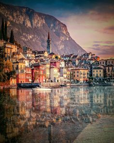 the city is reflected in the still water of the lake at sunset, with mountains in the background