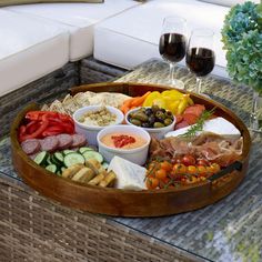 a wooden tray filled with different types of food and wine glasses on top of a table